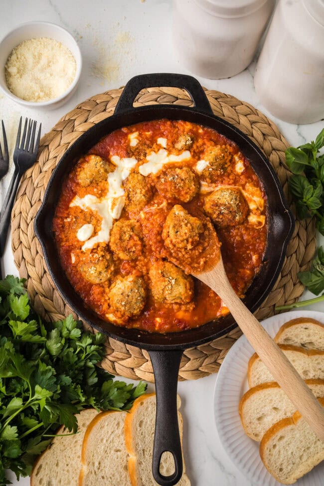 Chicken Parmesan meatballs simmering in marinara sauce in a cast iron skillet.