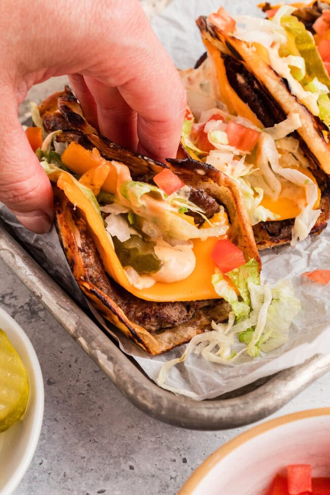 Smash burger tacos with melted cheese, burger sauce and fresh toppings being picked up