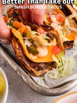 Smash burger tacos with melted cheese and toppings being picked up by hand