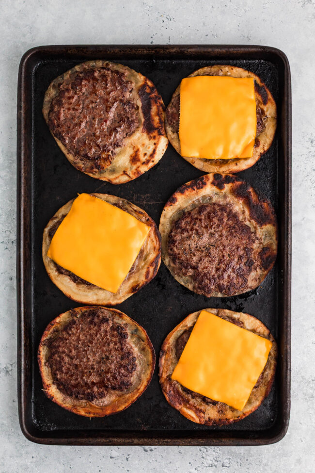 Smash burger tacos cooking in a skillet with beef pressed onto tortillas