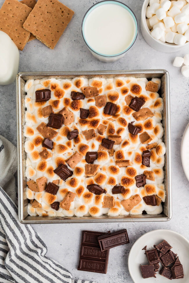 s’mores brownies in baking pan topped with toasted mini marshmallows, graham crackers, and chocolate pieces
