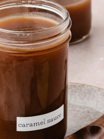 Homemade apple cider caramel sauce in a glass jar with a wooden spoon.