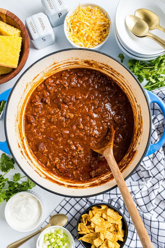 pot of easy cowboy chili in a blue dutch oven with chili toppings around for serving