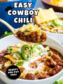 Close-up bowl of Easy Cowboy Chili topped with shredded cheddar cheese, sour cream, sliced jalapeños, and green onions.