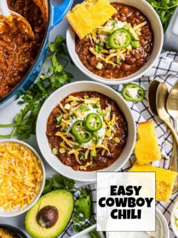 Overhead view of two bowls of Easy Cowboy Chili served with cornbread, shredded cheese, and fresh toppings.