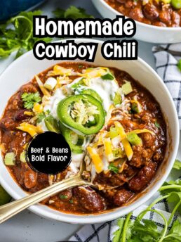 Close-up bowl of Easy Cowboy Chili topped with sour cream, shredded cheddar cheese, sliced jalapeños, and green onions.