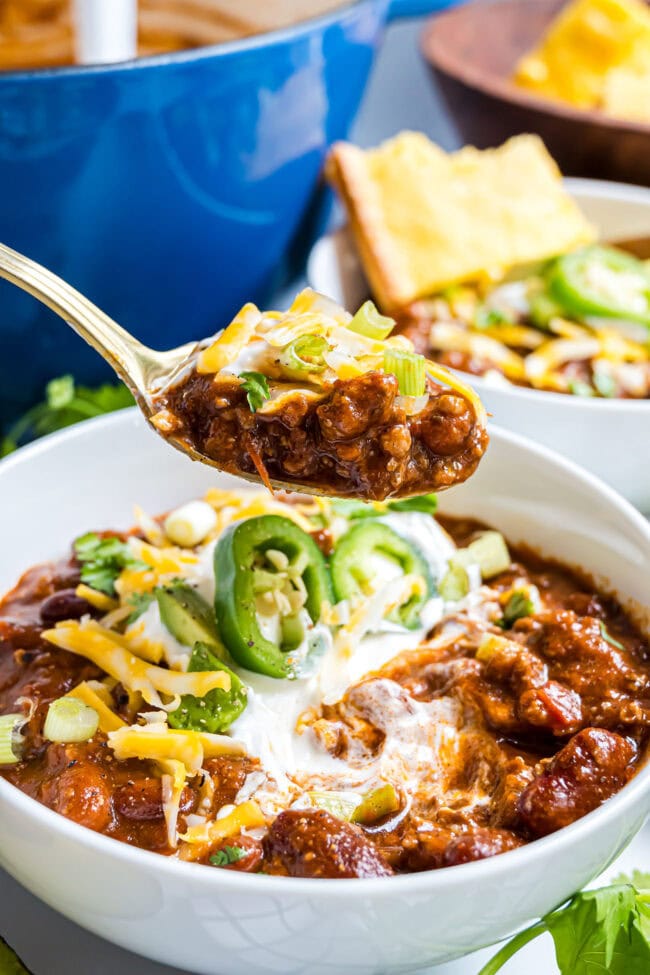 Spoonful of Easy Cowboy Chili with ground beef, pinto beans, kidney beans, and melted cheese over a bowl of chili topped with sour cream and jalapeños.