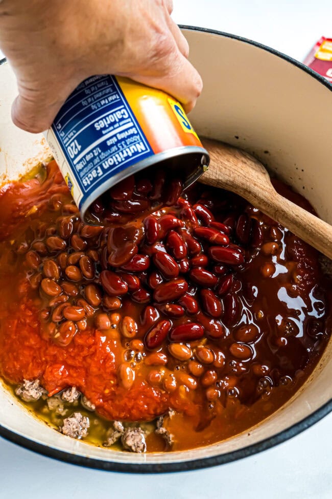 pouring a can of chili beans into a blue dutch oven for cowboy chili
