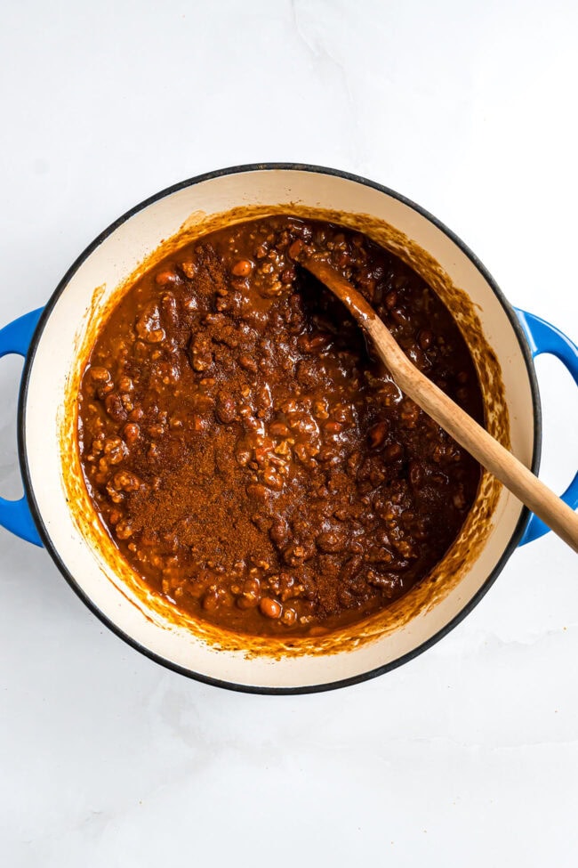 using a wooden spoon to stir chili seasoning into simmer pot of easy cowboy chili