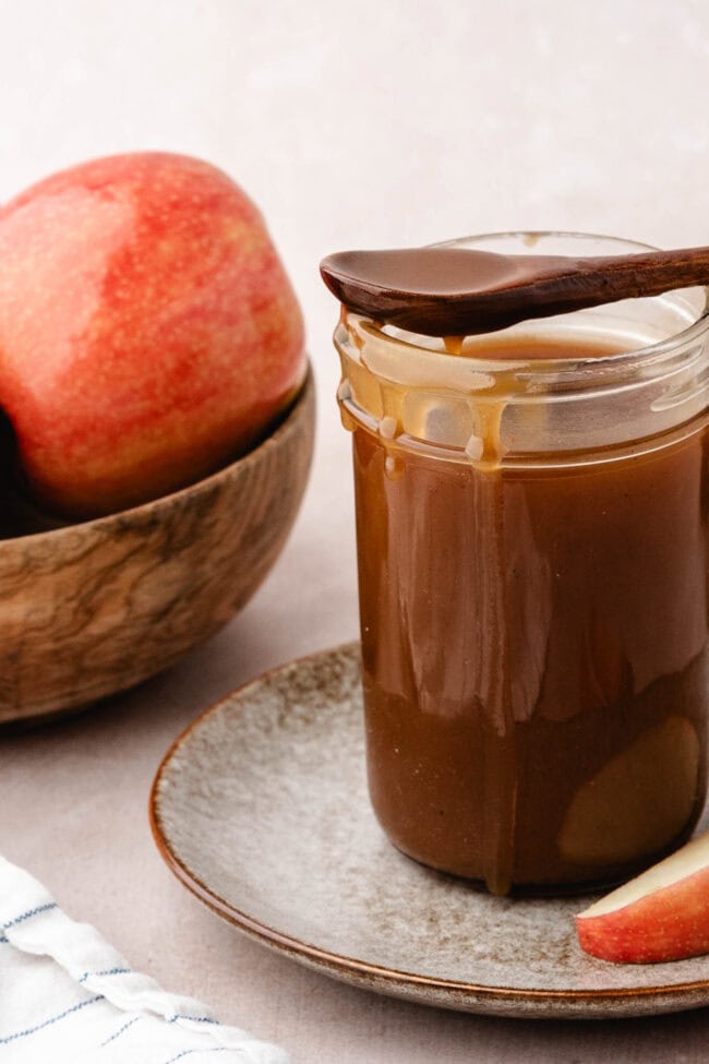 Homemade salted apple cider caramel sauce in a glass jar with fresh apples.