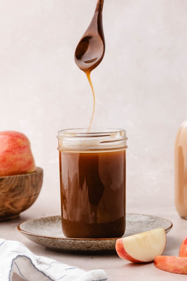 Homemade apple cider caramel sauce dripping from a spoon over a glass jar.