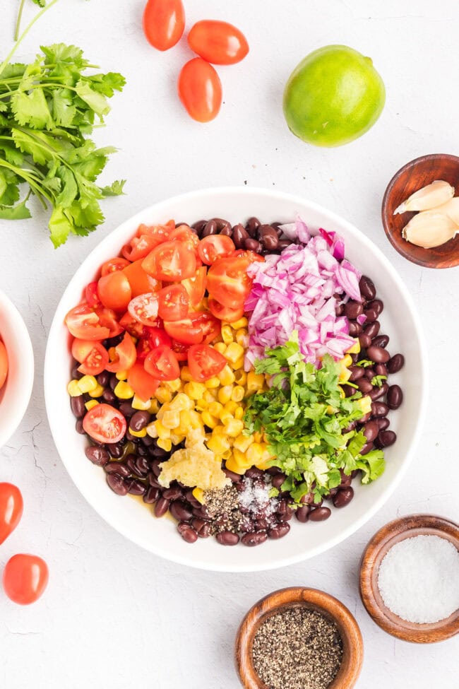 Combining black beans, corn, tomatoes, red onion, cilantro, and lime juice to make the Southwest salad.