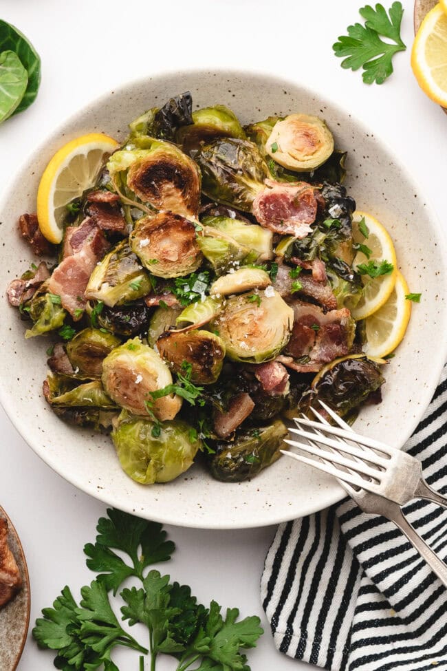 Maple bacon Brussels sprouts served on a plate with fresh lemon and parsley