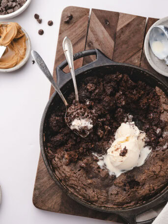 Chocolate cobbler in a skillet with vanilla ice cream and a spoonful lifted from the center