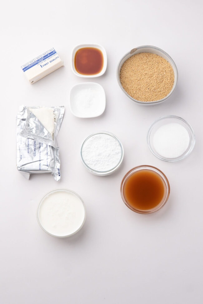 Cream cheese, heavy cream, graham crackers, sugar, vanilla, and caramel sauce arranged for the recipe.