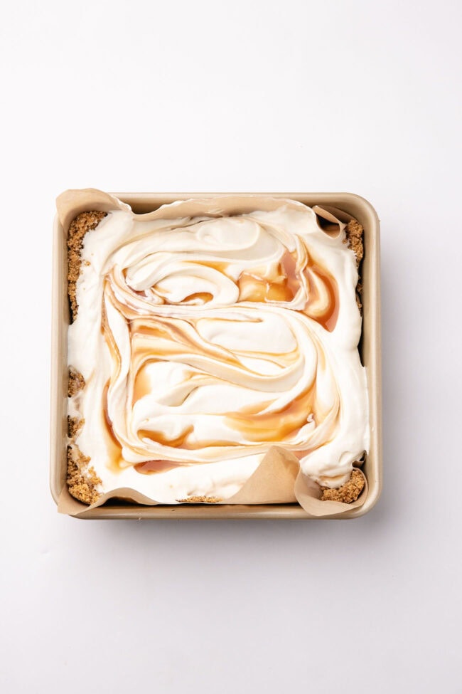 No-bake cheesecake filling topped with swirls of salted caramel in a square baking dish