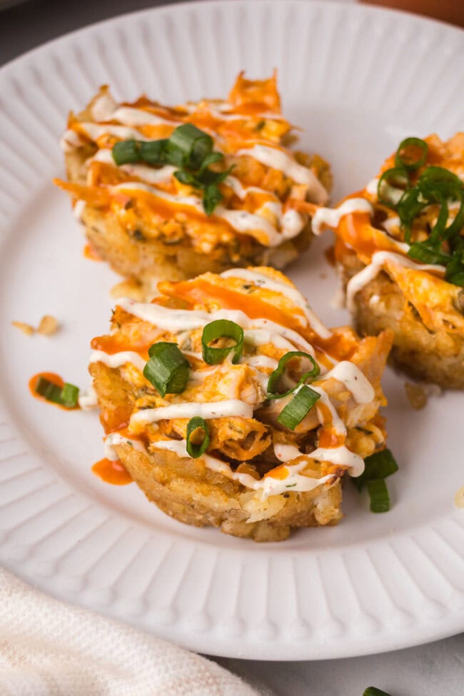 Buffalo chicken tater tot cups topped with ranch drizzle and sliced green onions on a white plate.