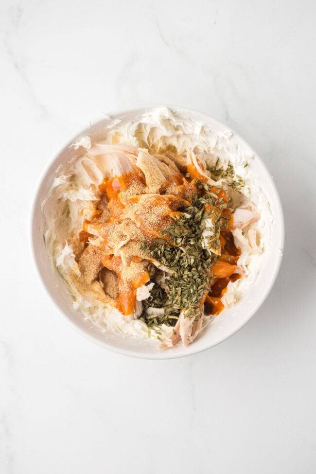 Shredded chicken, cream cheese, buffalo sauce, garlic powder, and dried chives in a bowl before mixing.