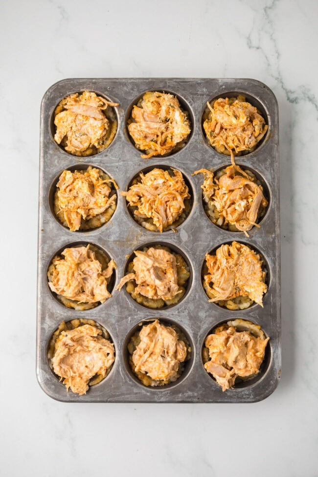 Muffin pan filled with tater tot cups and buffalo chicken filling before baking.