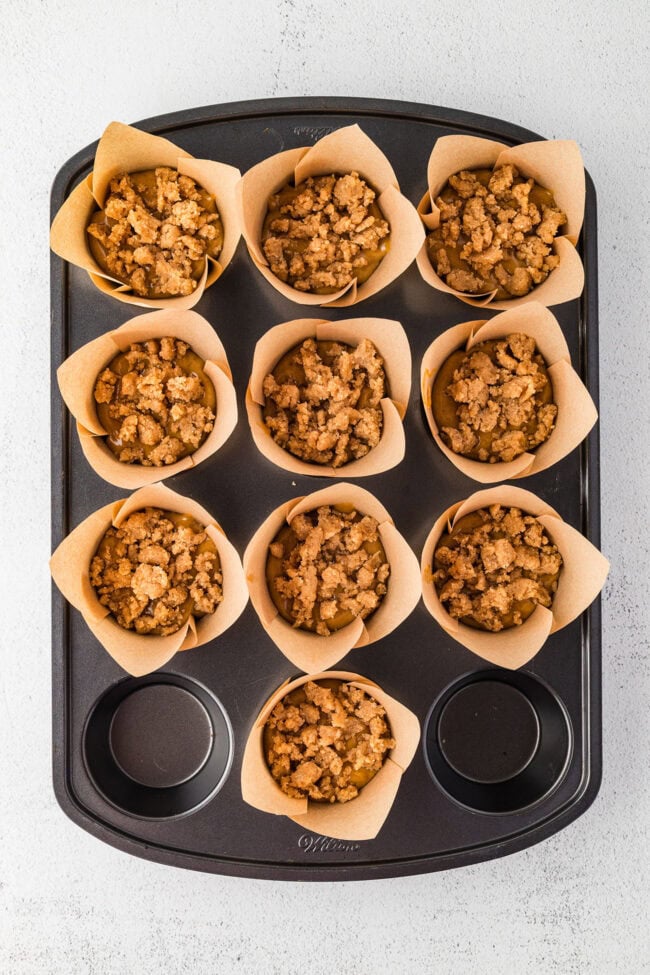 Gingerbread muffin batter in paper liners topped with spiced crumble before baking.