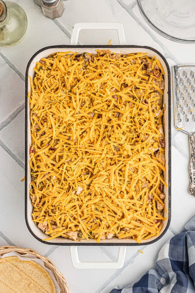 Assembled King Ranch chicken casserole topped with shredded cheddar cheese before baking.