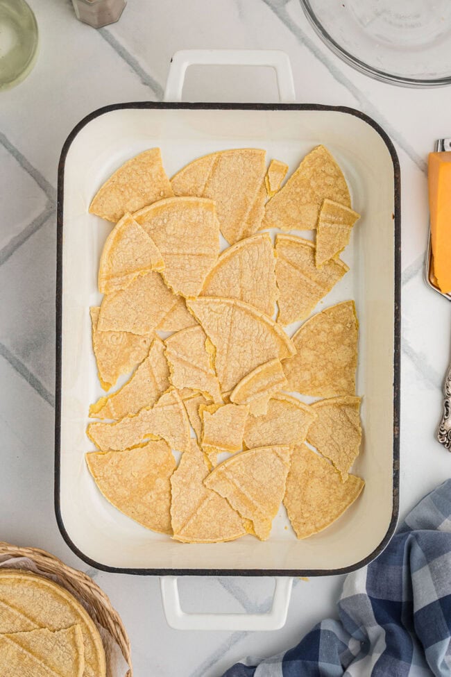 Torn corn tortillas covering the bottom of a white casserole dish.